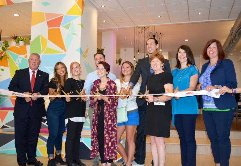 Employees stand with Albany Mayor and BID representatives holding a ribbon for their ribbon cutting ceremony