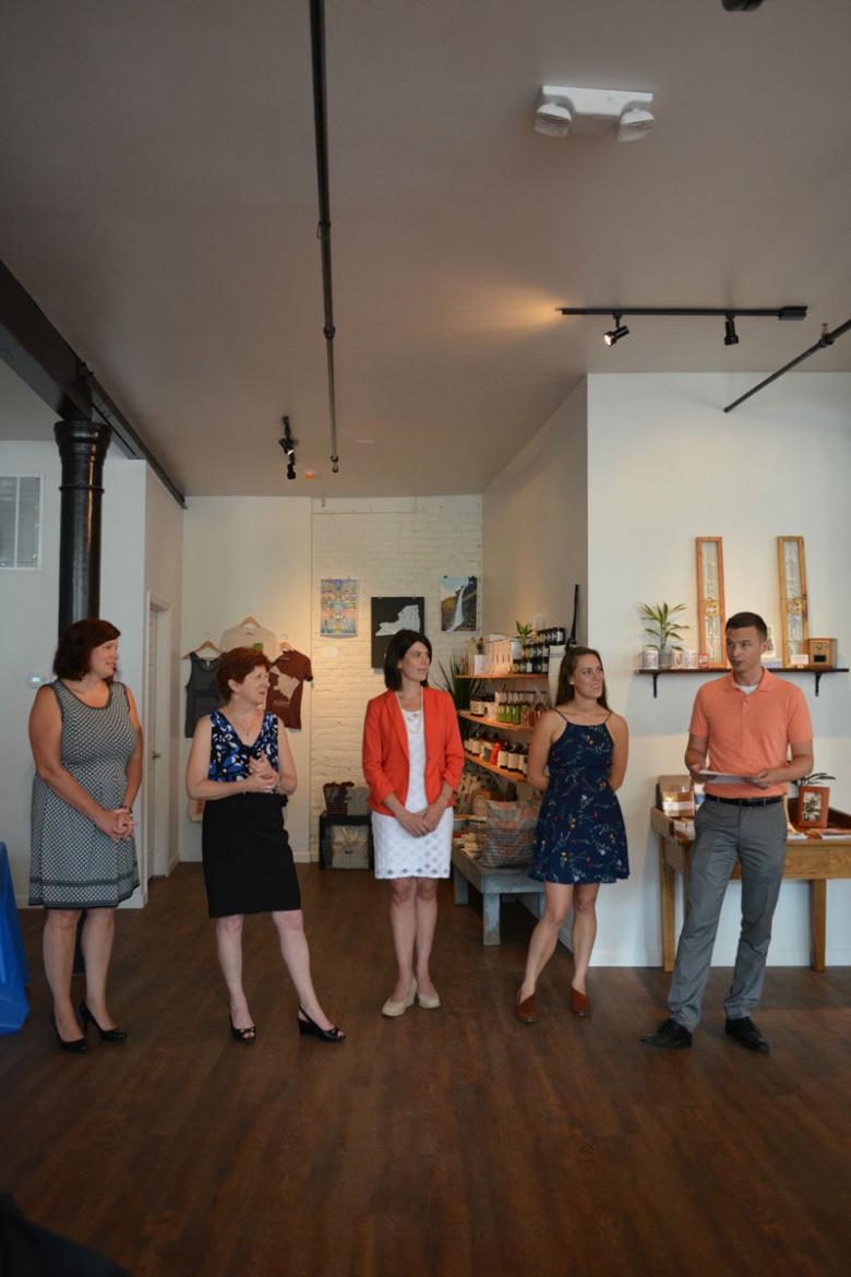 5 store employees stand in an empty back part of the store, addressing the crowd that came to welcome them on their grand opening