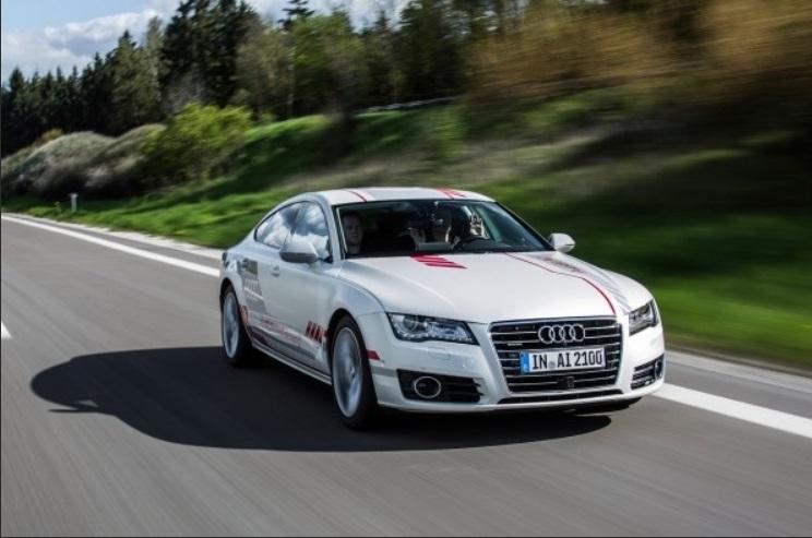 Action shot of a white Audi car on a road, background blurred to indicate speed, the driver raising both hands to show they are not on the steering wheel. 