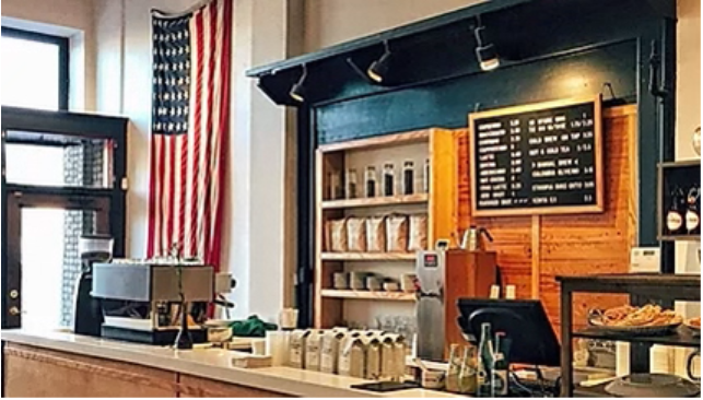 Interior of a business, looking at the counter with the register. A large american flag is hung from the wall near the front door. 